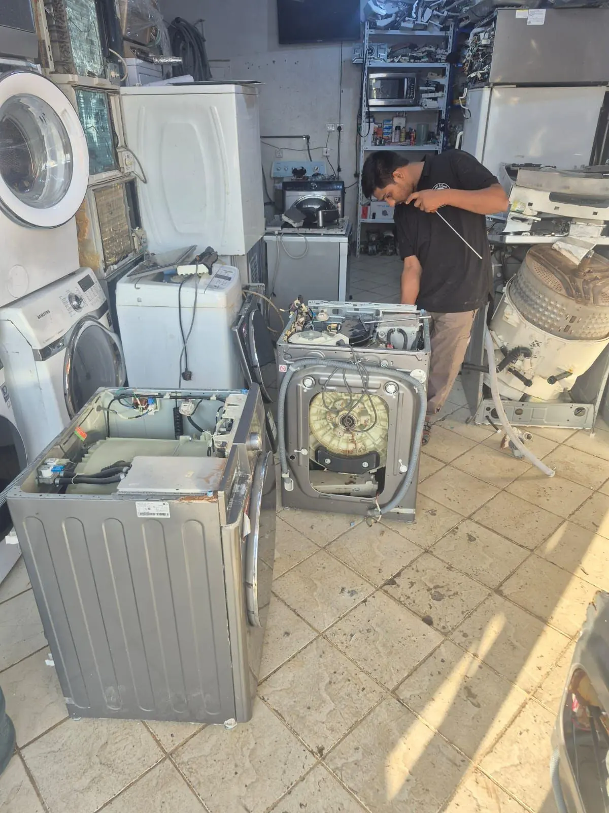 Repair workshop with several washing machines and a technician at work